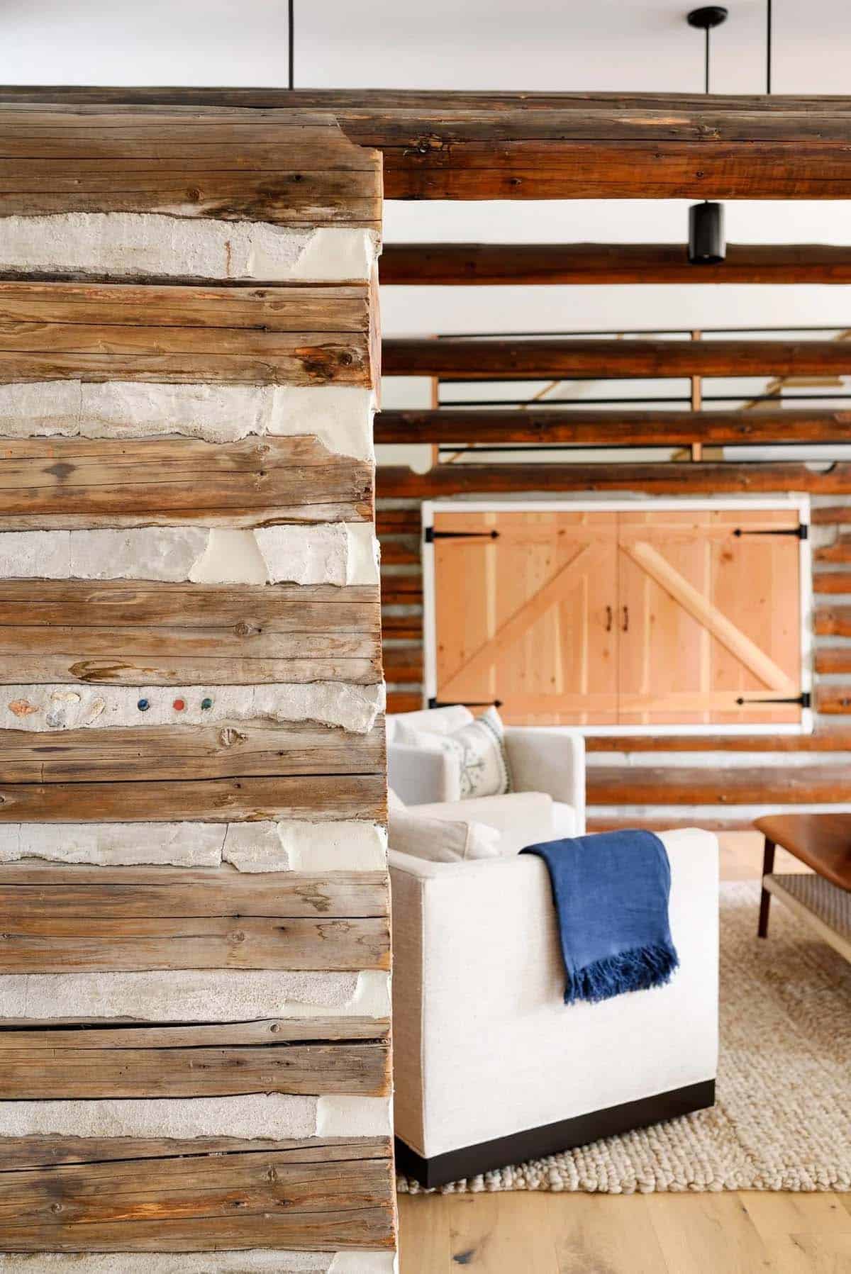 Detail of chinked log wall opening into a living room with a wooden barn-style door