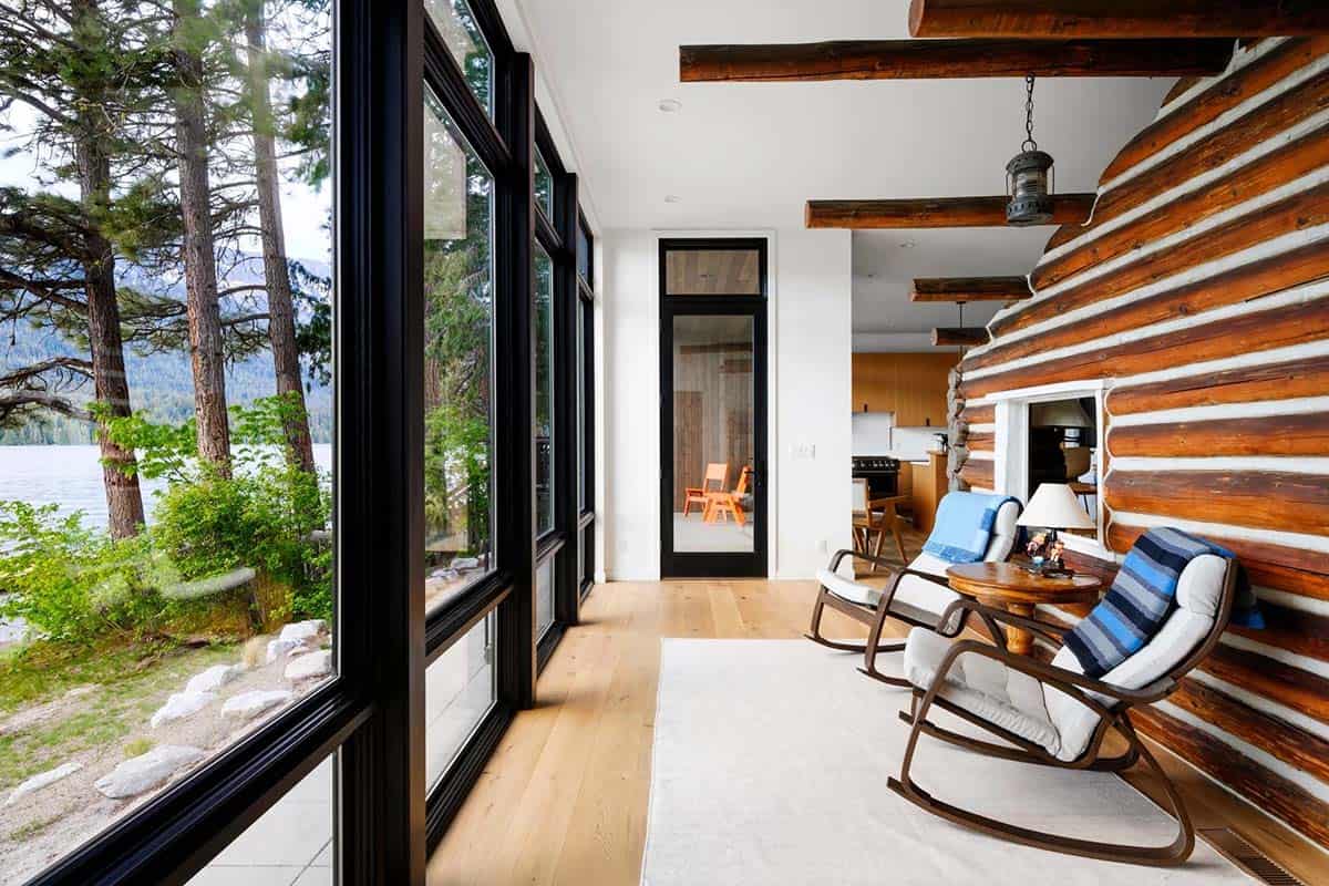 Sunroom with wraparound windows, rocking chairs, and a log cabin wall with built-in fireplace