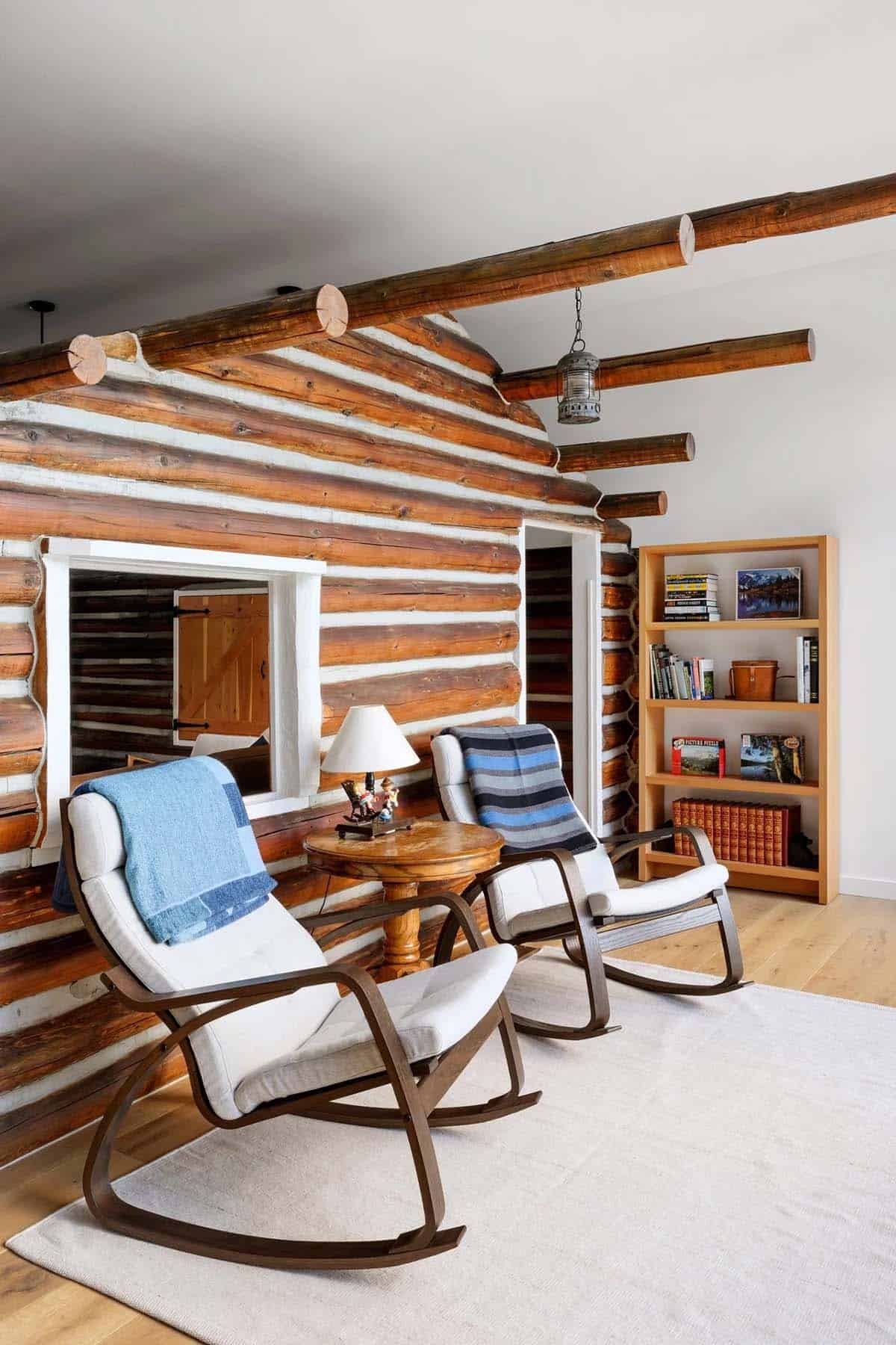 Cozy reading nook with two rocking chairs against a log cabin wall and built-in bookshelf