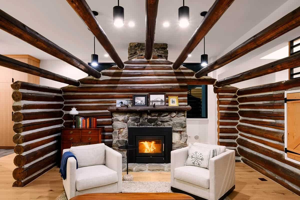 Living room fireplace nook framed by log walls, stone surround, and exposed ceiling beams