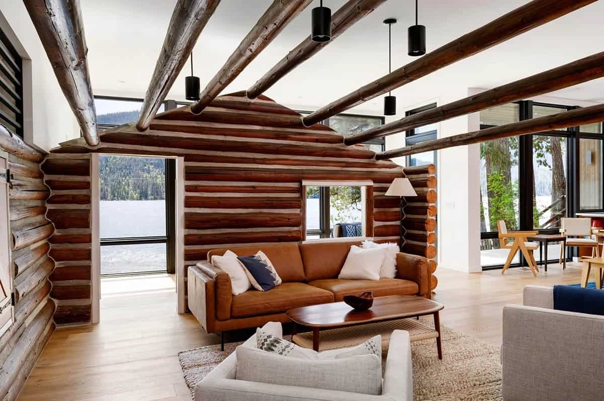 Living room with tan leather sofa against log cabin wall, lake visible through doorway
