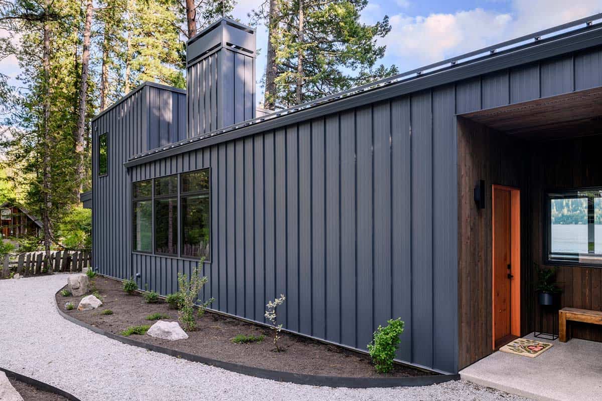 Angled exterior view of gray metal-clad cabin with wood-clad entry porch and orange front door