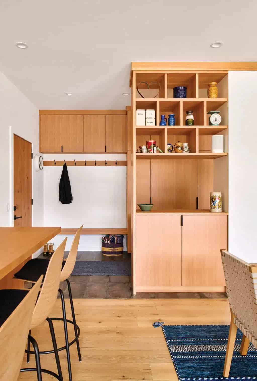 Mudroom nook with coat hooks, wood cubby shelving, and dining table with woven chairs