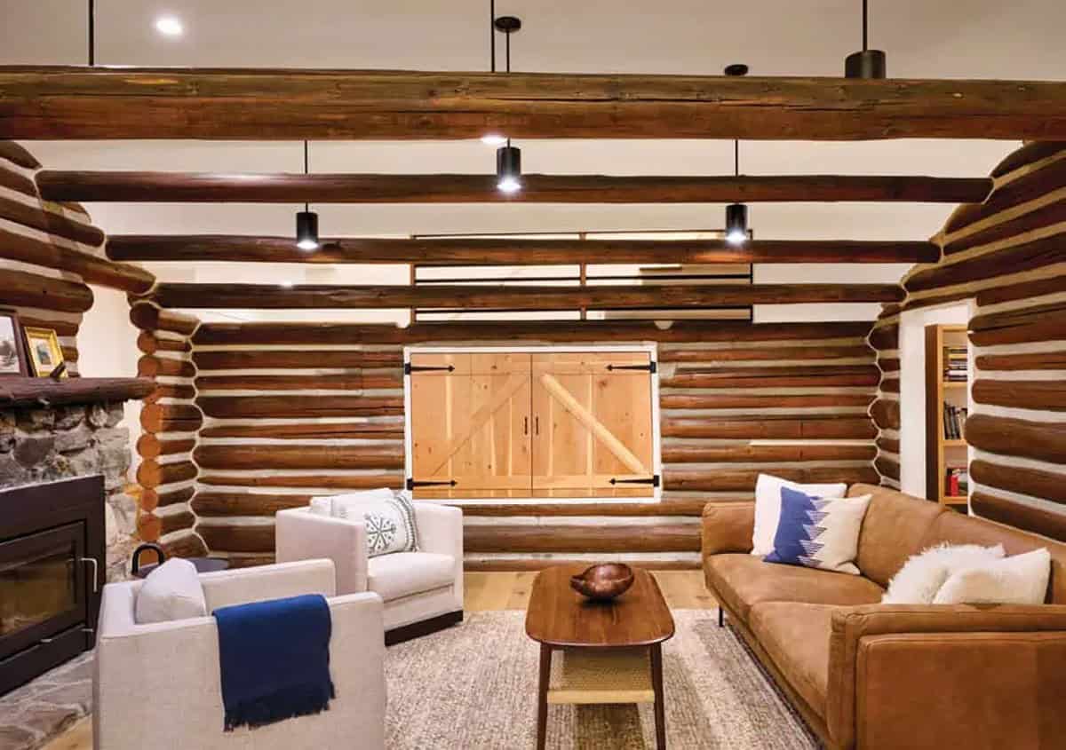 Living room with log cabin walls, exposed beams, stone fireplace, and barn-door style window shutter