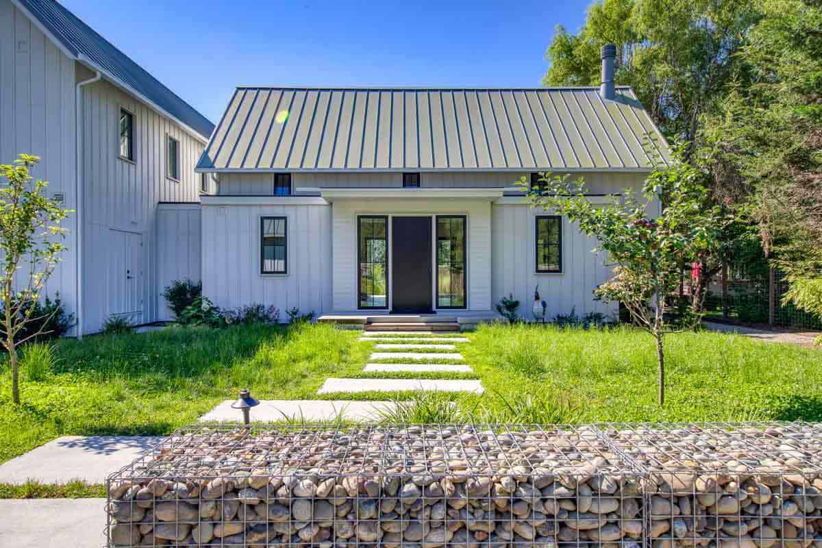 Front exterior of white board-and-batten farmhouse with metal gable roof and black entry door