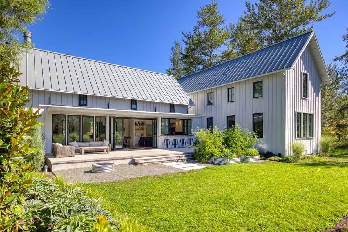 Rear view of the house with open bi-fold glass doors leading to a covered patio and gravel yard
