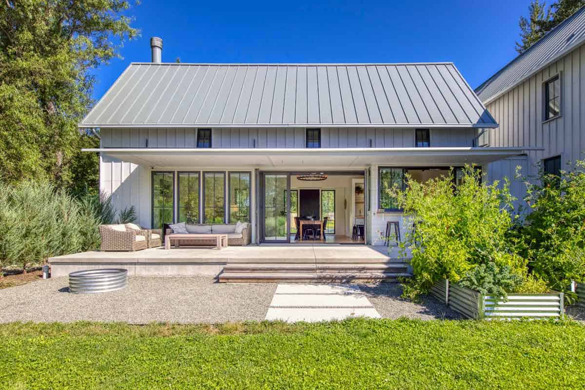 Symmetrical rear facade with metal roof, open folding doors, and covered patio seating area