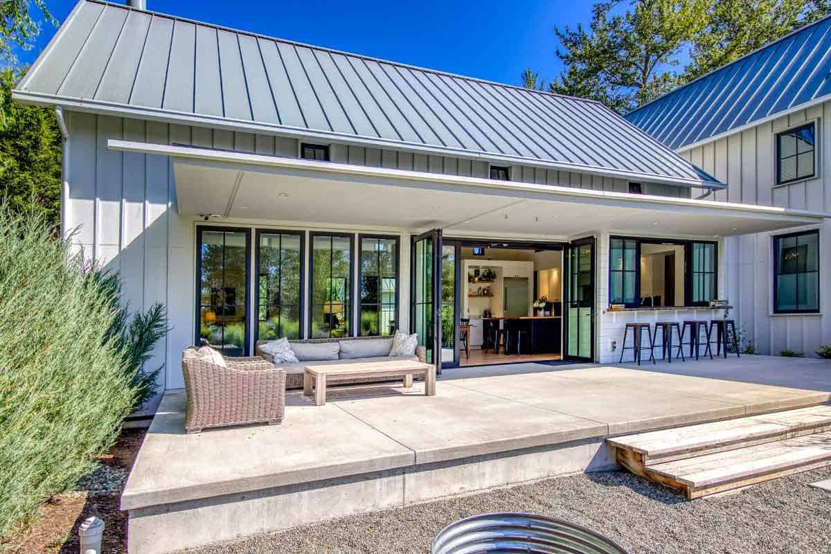 Covered patio with wicker furniture beside open folding glass doors and a pass-through bar window