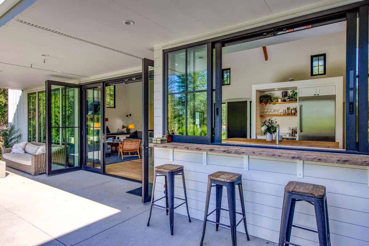 Patio bar with wooden countertop and stools beneath an open pass-through kitchen window