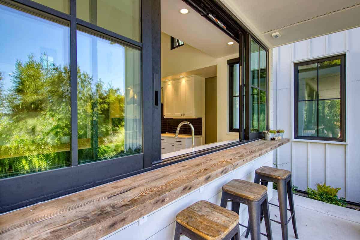 Interior view through an open sliding kitchen window to a white farmhouse-style kitchen