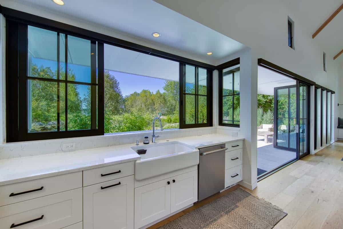 Kitchen sink area with black-framed windows overlooking greenery and an open sliding glass door