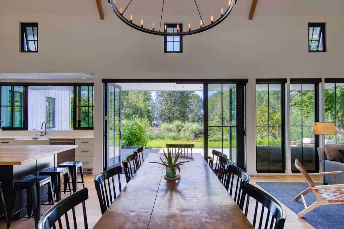 Open-concept dining area with long wooden table, black chairs, and wheel chandelier, opening to the patio
