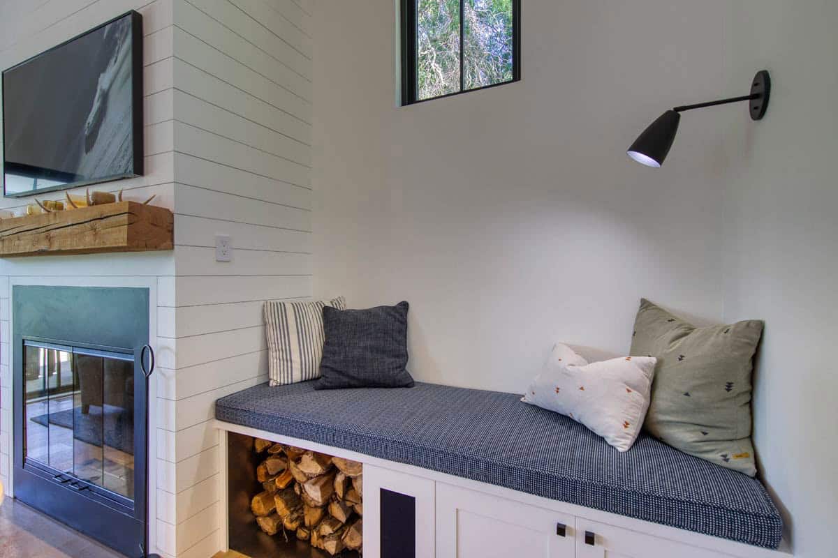 Close-up of built-in window seat with striped and patterned pillows above a firewood storage nook