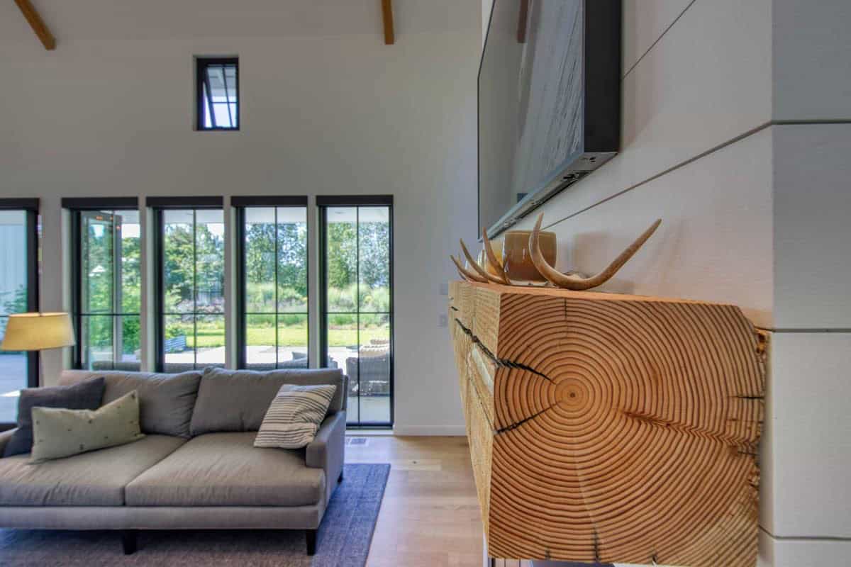 Reclaimed wood mantel with antler decor beside a gray sofa and wall of black-framed windows