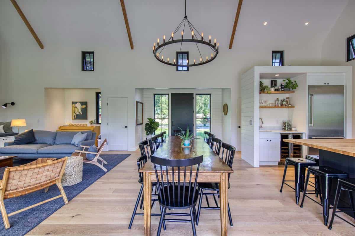 Open-concept dining and living area with wood table, wheel chandelier, and view to the front entry