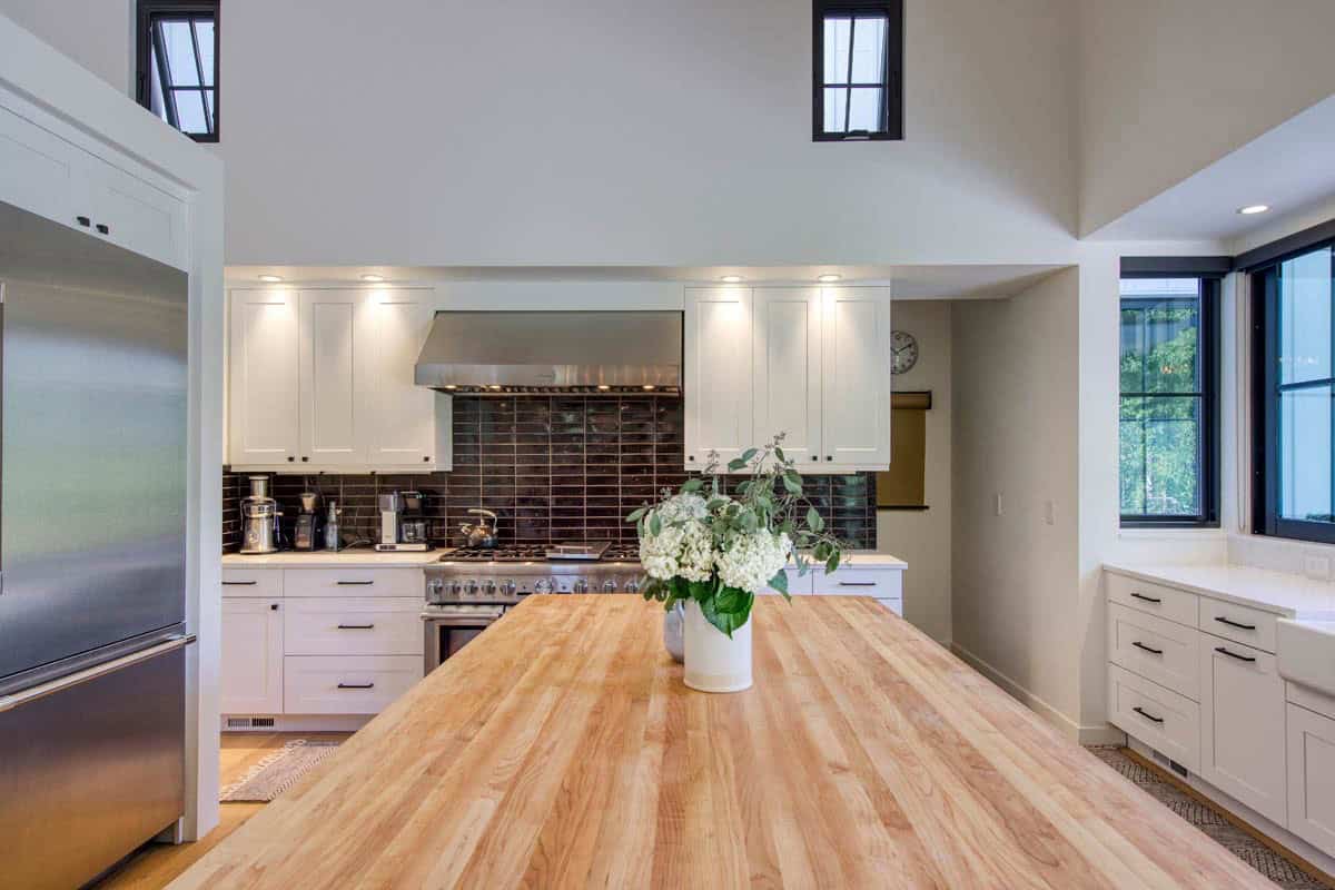 Kitchen with white shaker cabinets, black tile backsplash, stainless range, and butcher-block island