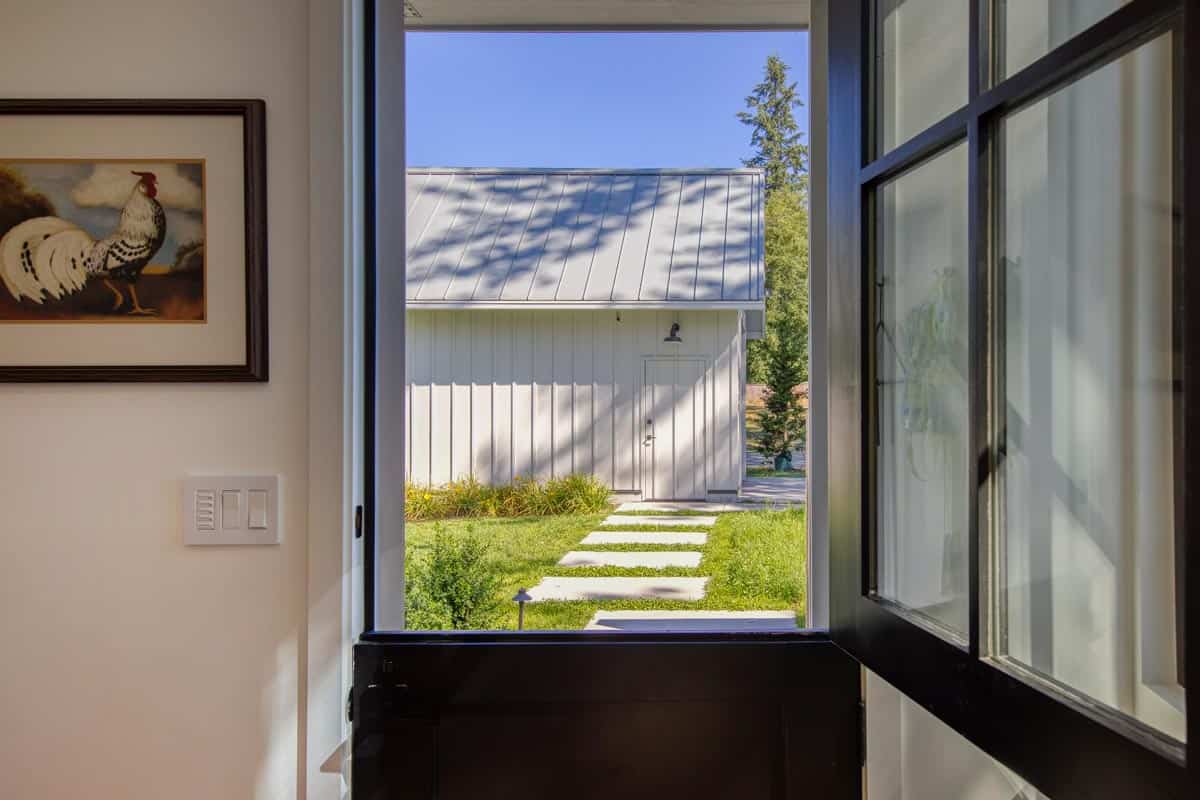 View through an open black-framed Dutch door to a courtyard and outbuilding