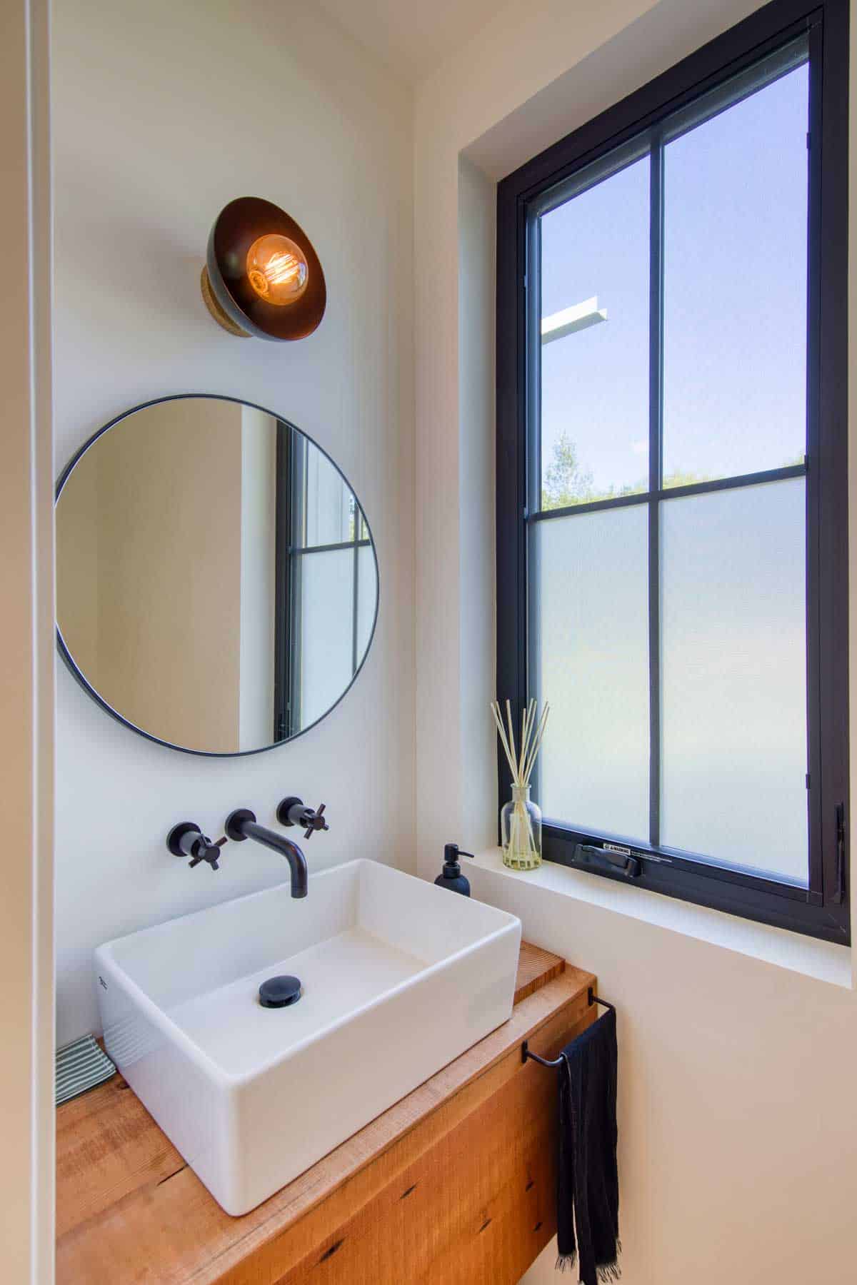 Powder room with round mirror, black wall-mount faucet, vessel sink, and frosted window