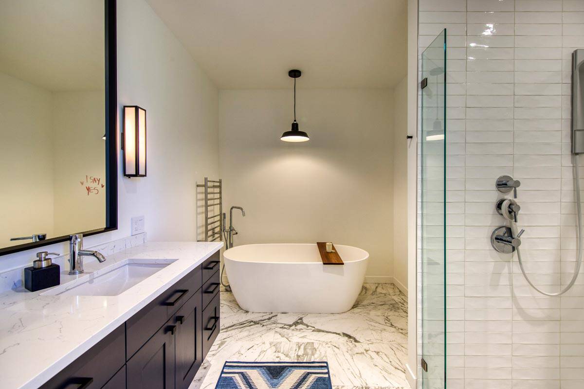 Primary bathroom with freestanding tub, marble floor, dark vanity, and glass-enclosed shower