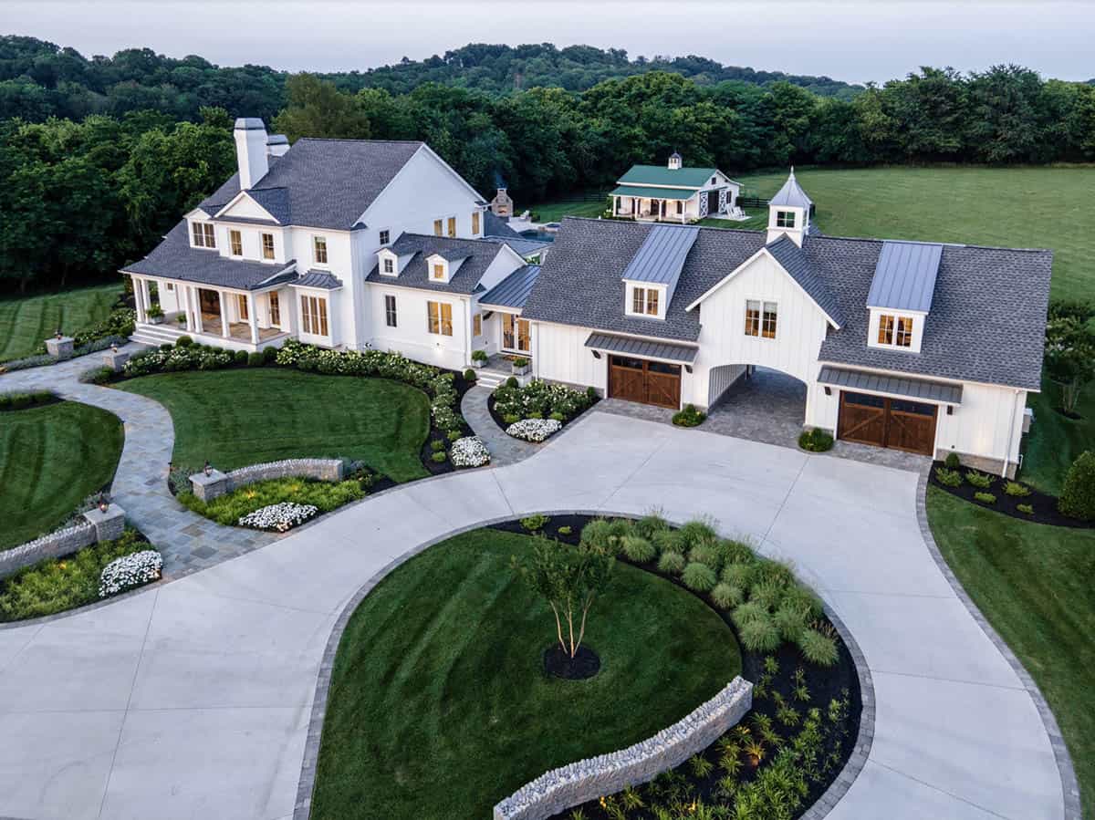 Aerial view of a white modern farmhouse estate with circular driveway and landscaped lawn