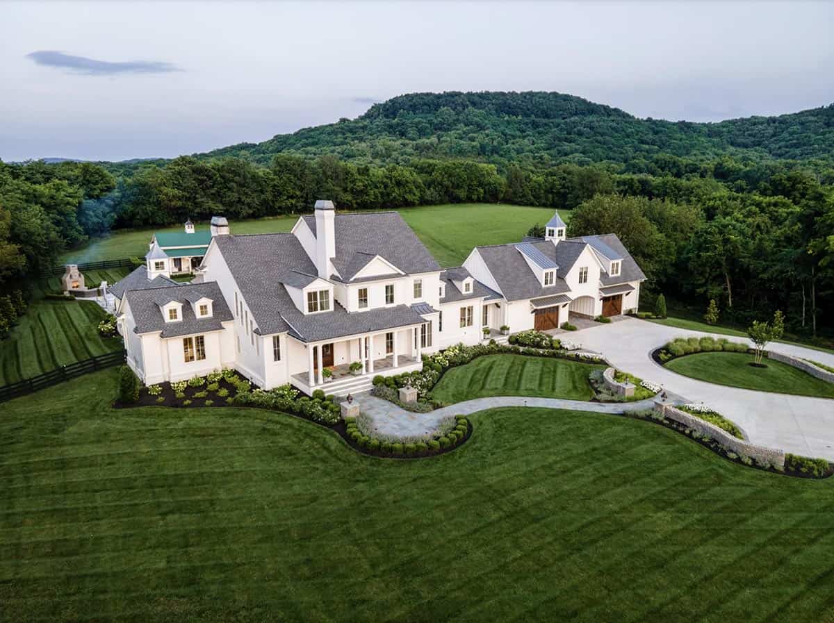Aerial view of the farmhouse estate with rolling green hills and forest in the background