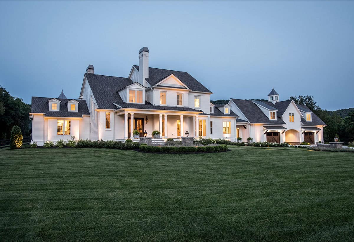 Twilight view of the illuminated white farmhouse exterior with wraparound porch