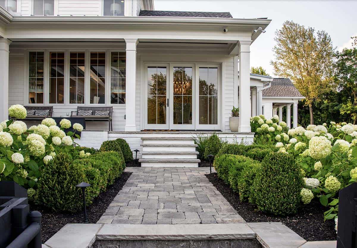 Covered porch entrance with French doors, hydrangeas, and stone pathway