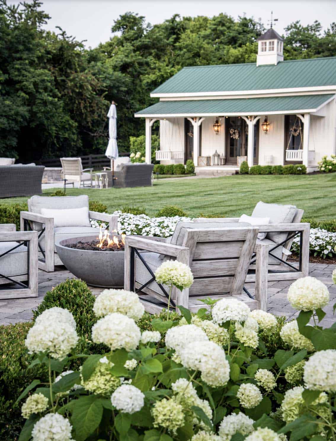 Fire pit lounge area with hydrangeas and green-roofed pool house in background