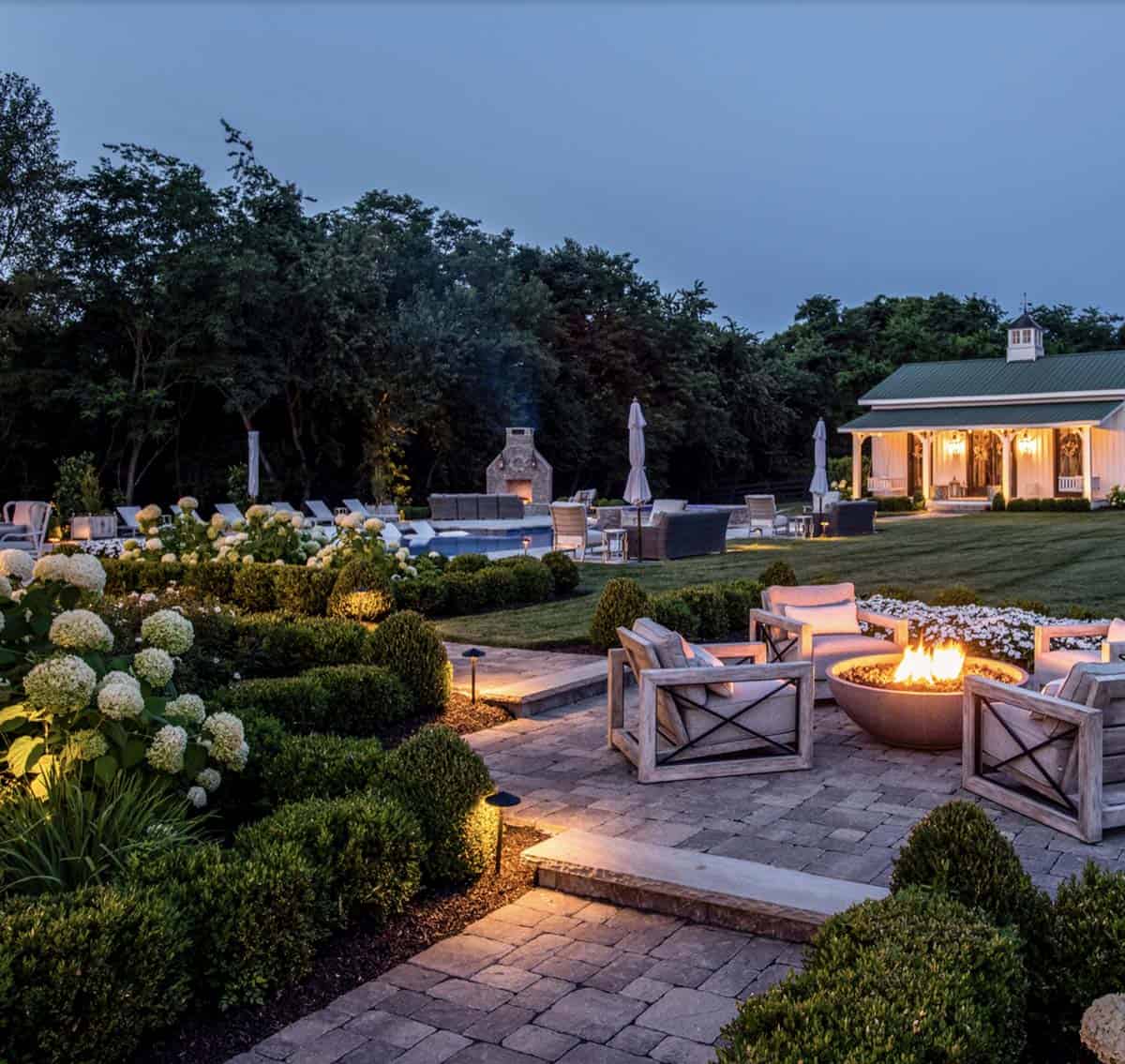 Twilight view of the backyard with fire pit, pool, and lit pool house