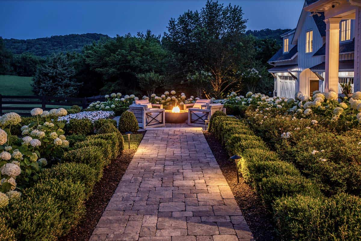 Nighttime paver pathway leading to a lit fire pit lounge area