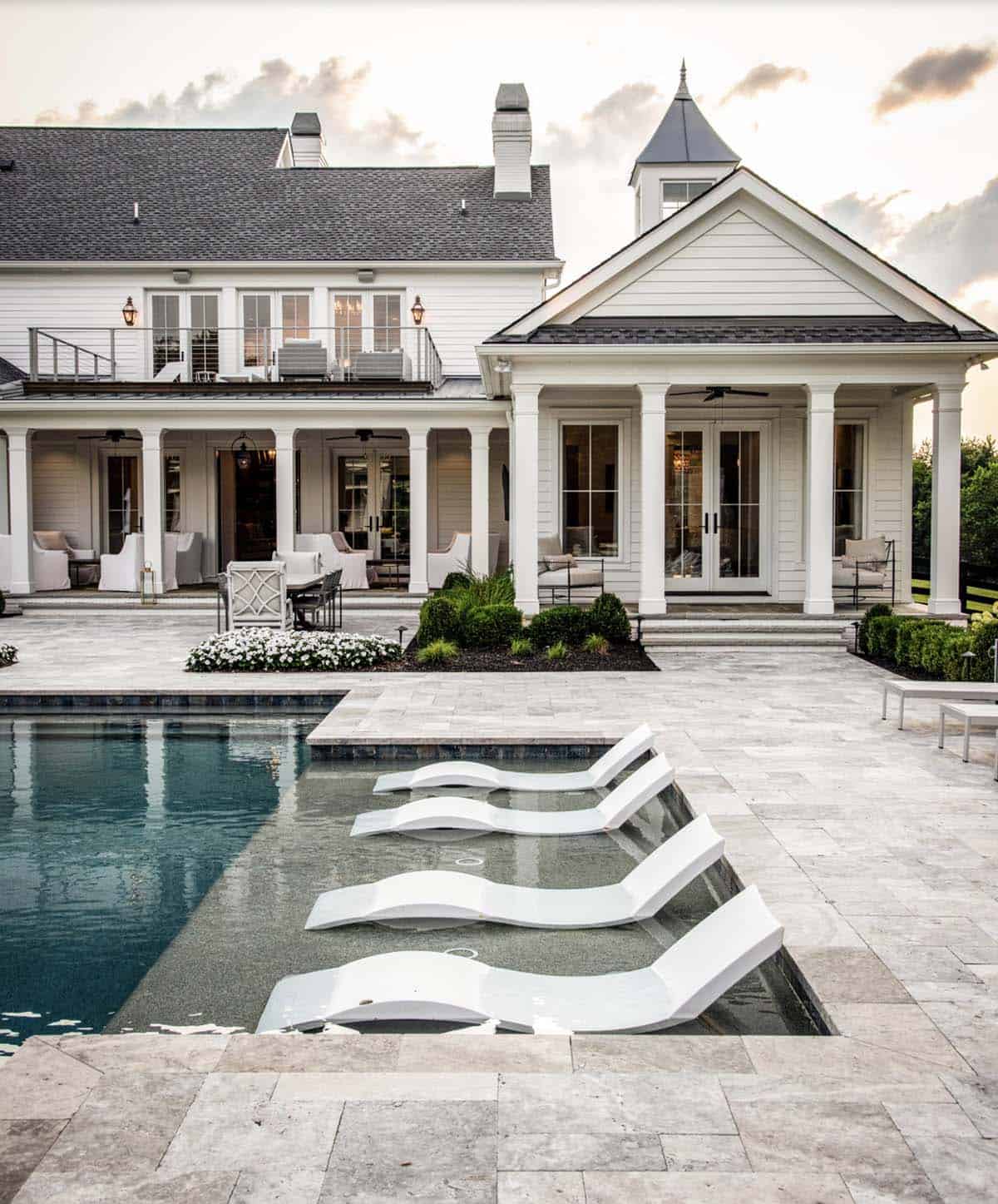 Pool deck with in-water lounge chairs and columned porch of the main house