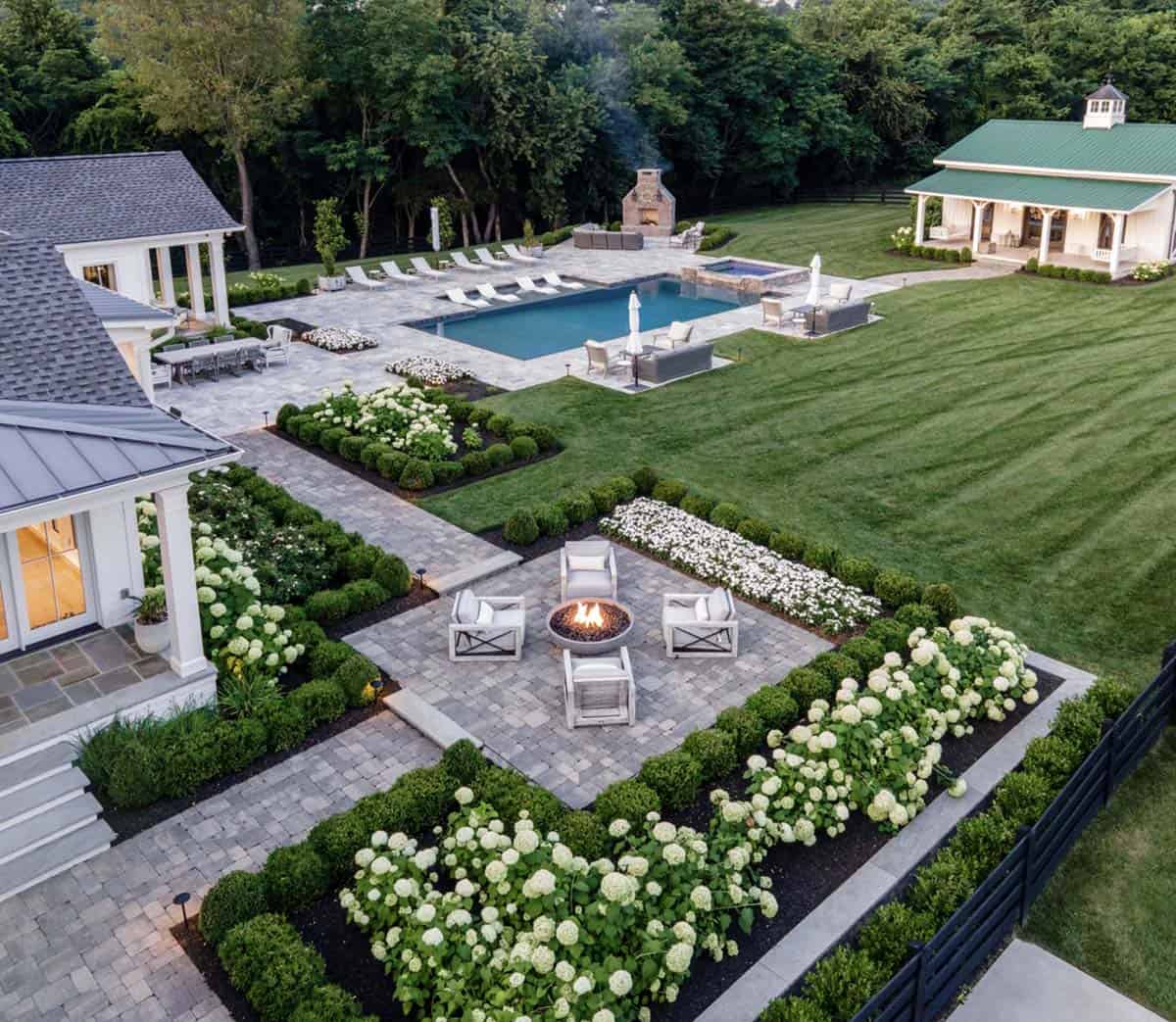Aerial view of the backyard patio, fire pit, pool, and green-roofed pool house at dusk