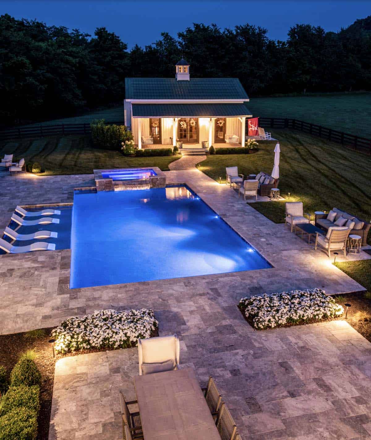 Nighttime view of the illuminated pool, spa, and pool house