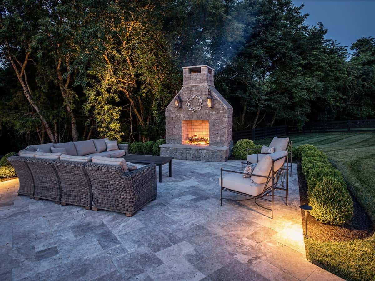 Outdoor stone fireplace with wicker sectional and lounge chairs at dusk