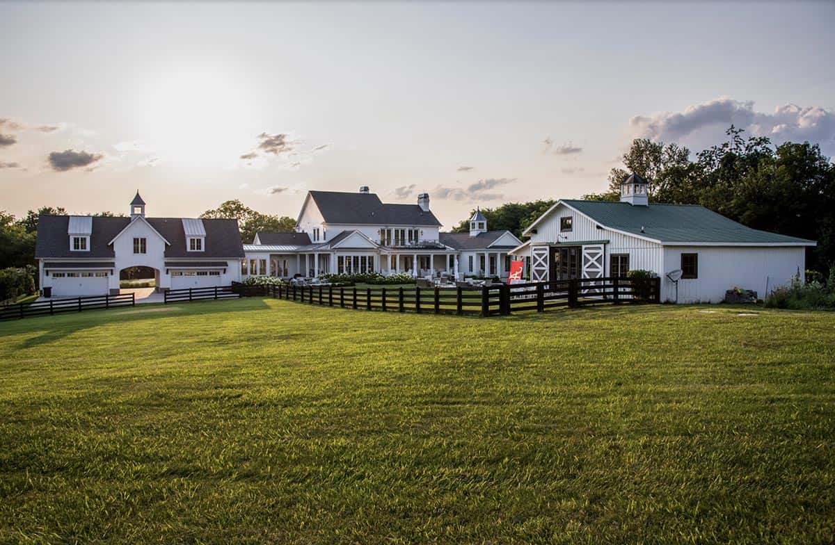 Wide view of the estate showing garage, main house, and barn connected by black fencing