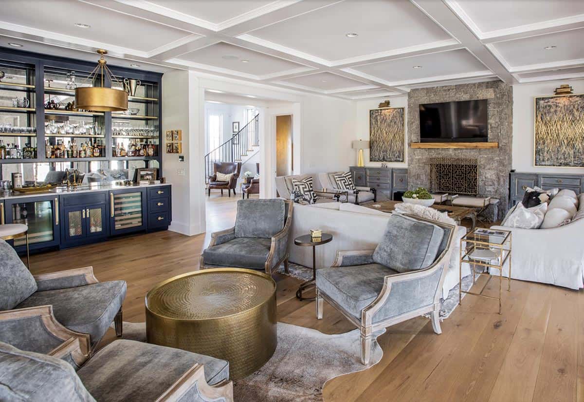 Living room with navy built-in bar, stone fireplace, and gray velvet armchairs