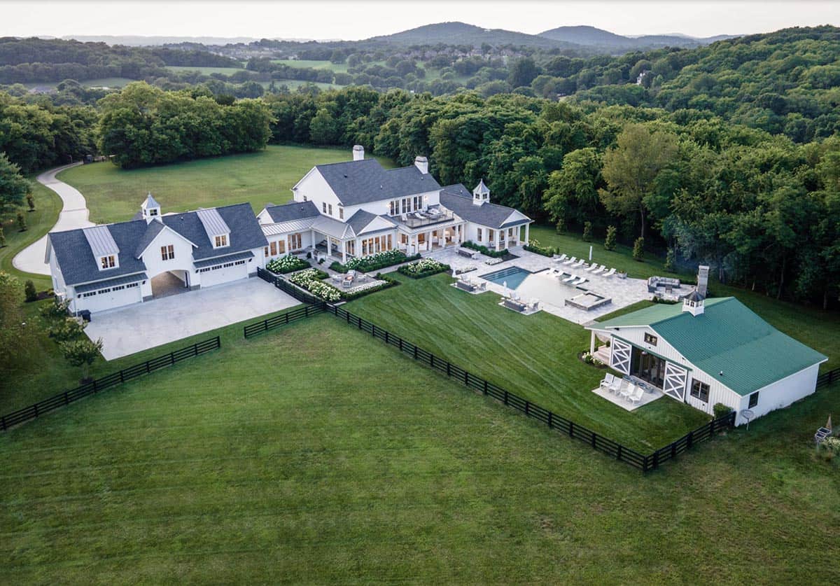 Aerial view of the full estate with main house, garage, pool, and pool house amid rolling hills