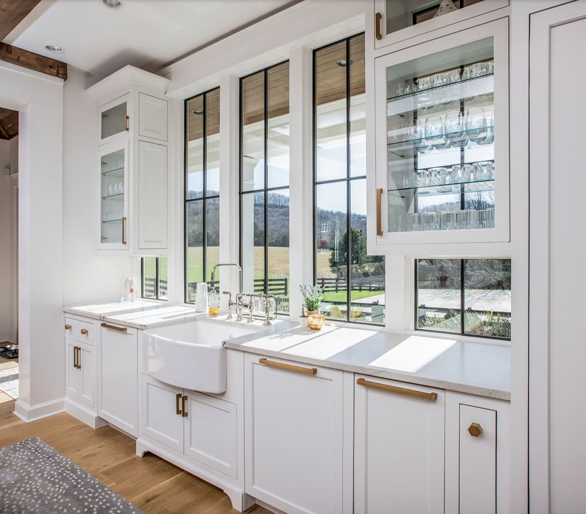 Butler's pantry with farmhouse sink, glass cabinetry, and pastoral window views