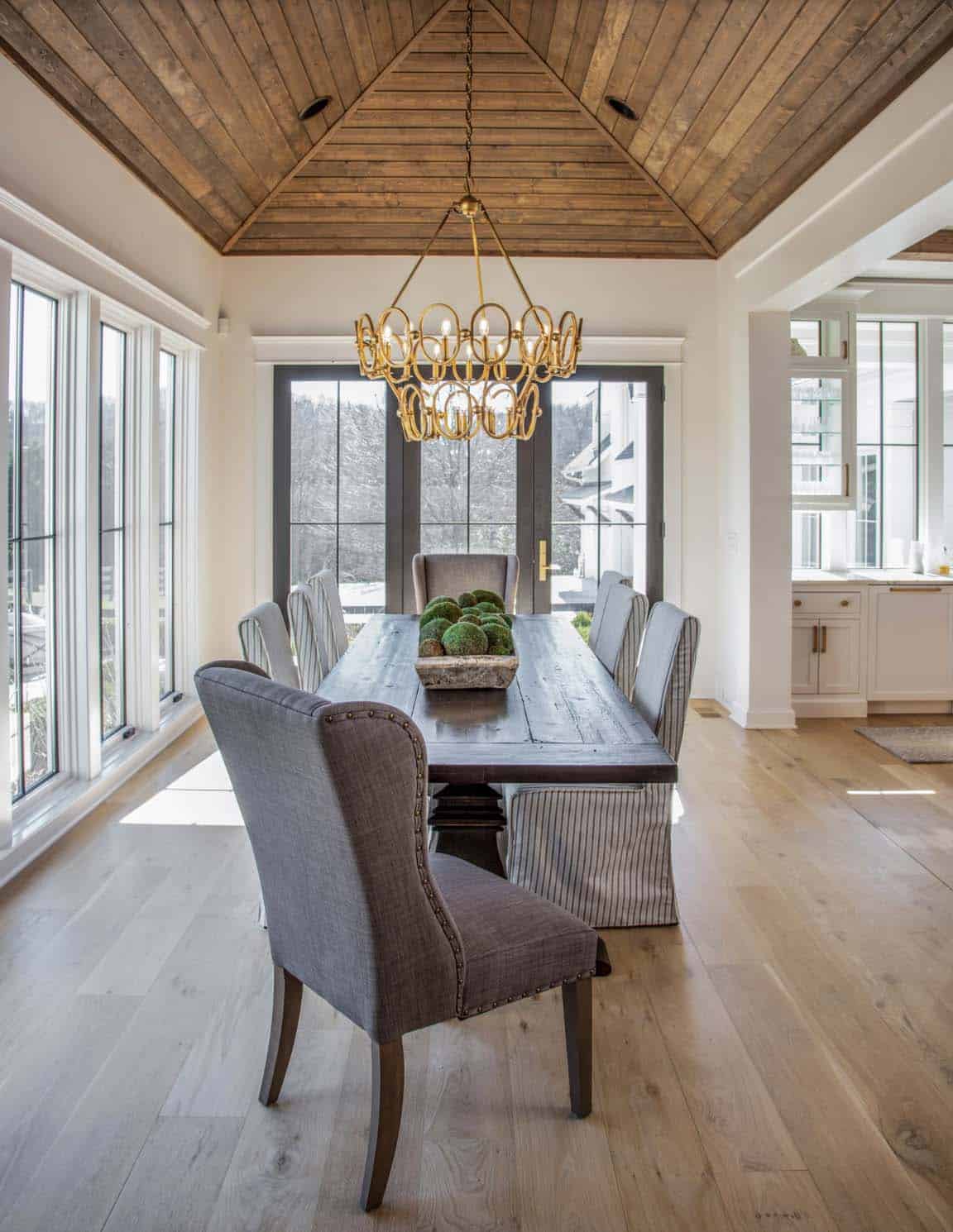 Dining nook with wood-clad vaulted ceiling, brass chandelier, and striped chairs