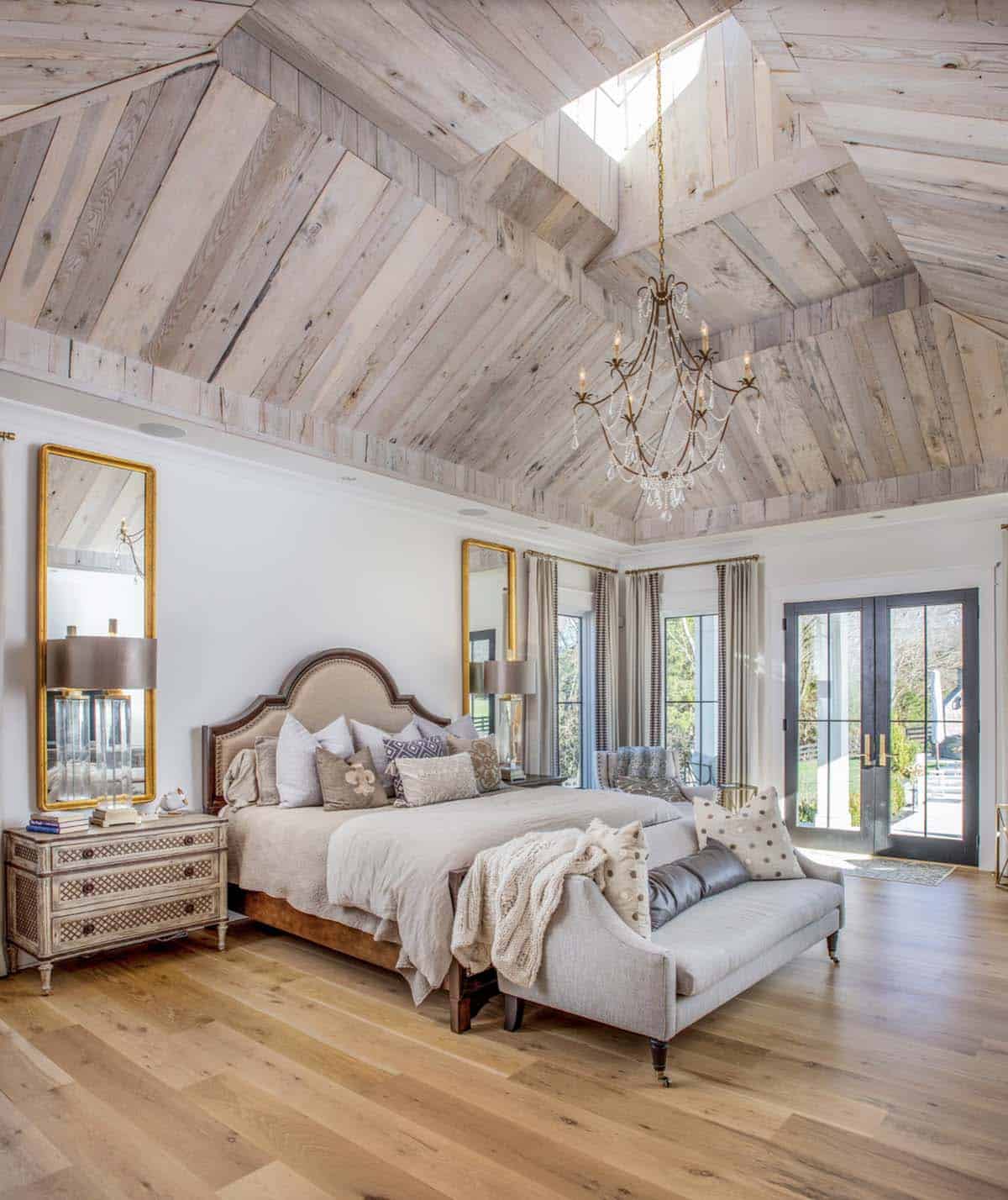 Primary bedroom with rustic wood vaulted ceiling, skylight, and crystal chandelier