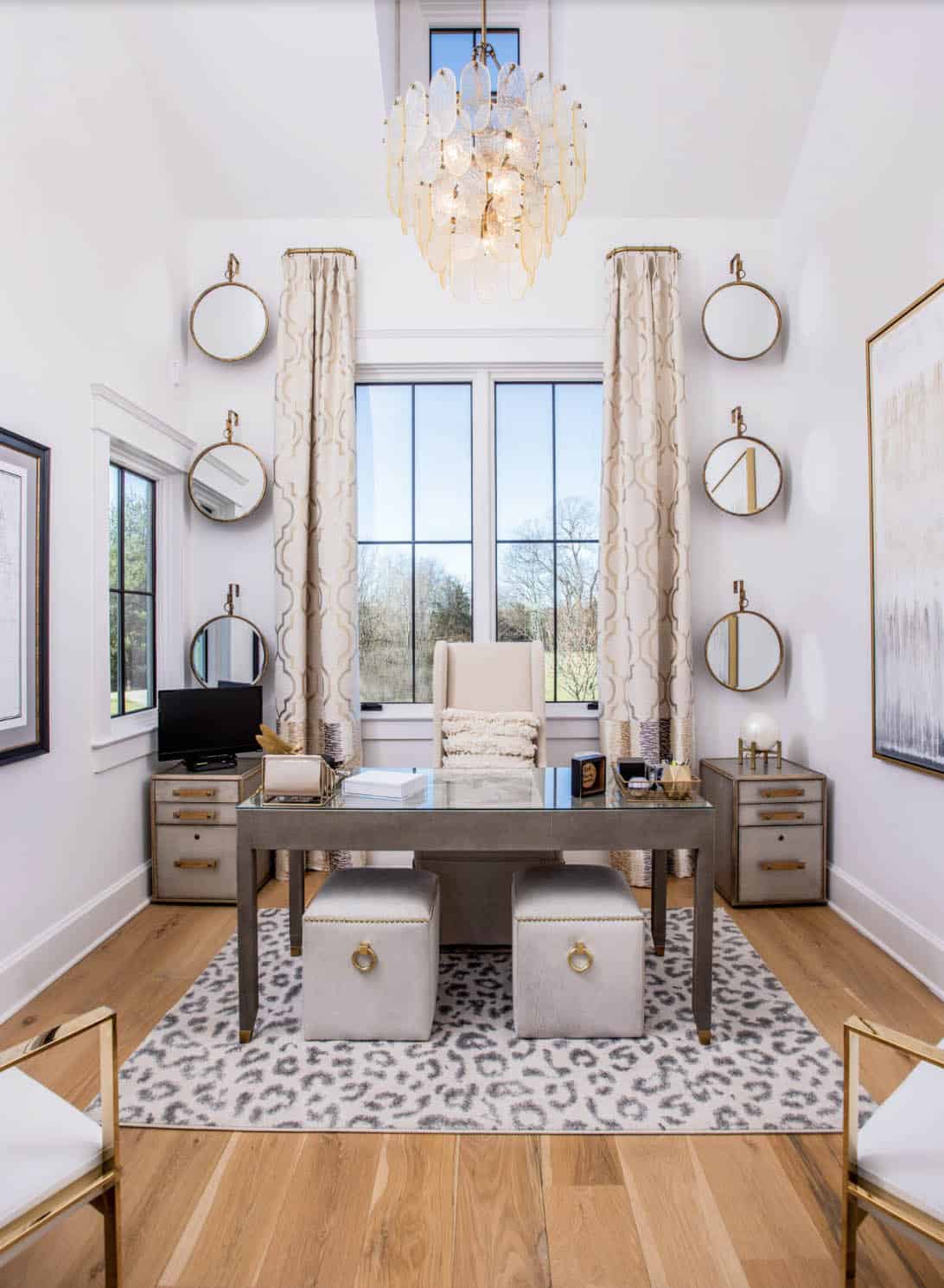 Home office with glass desk, round mirrors, and dramatic glass-drop chandelier