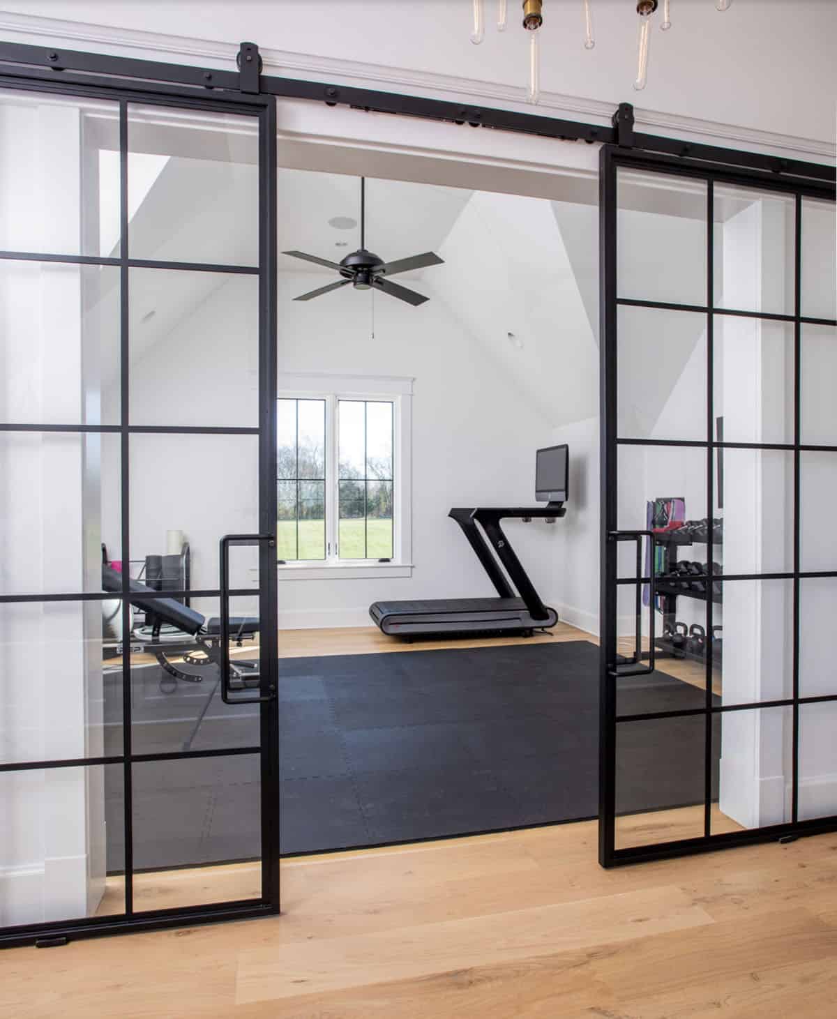 Home gym with black-framed glass sliding doors, treadmill, and workout equipment