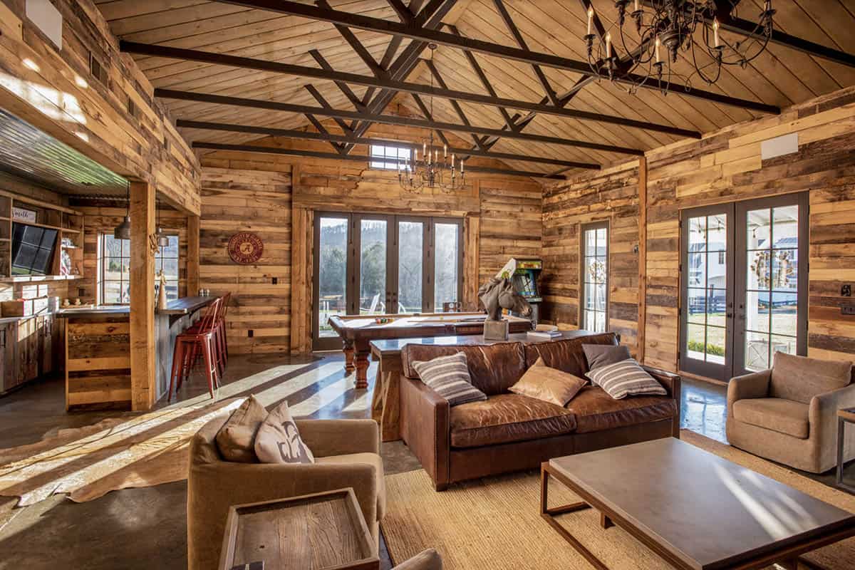 Rustic barn recreation room with pool table, leather sofa, and timber trusses