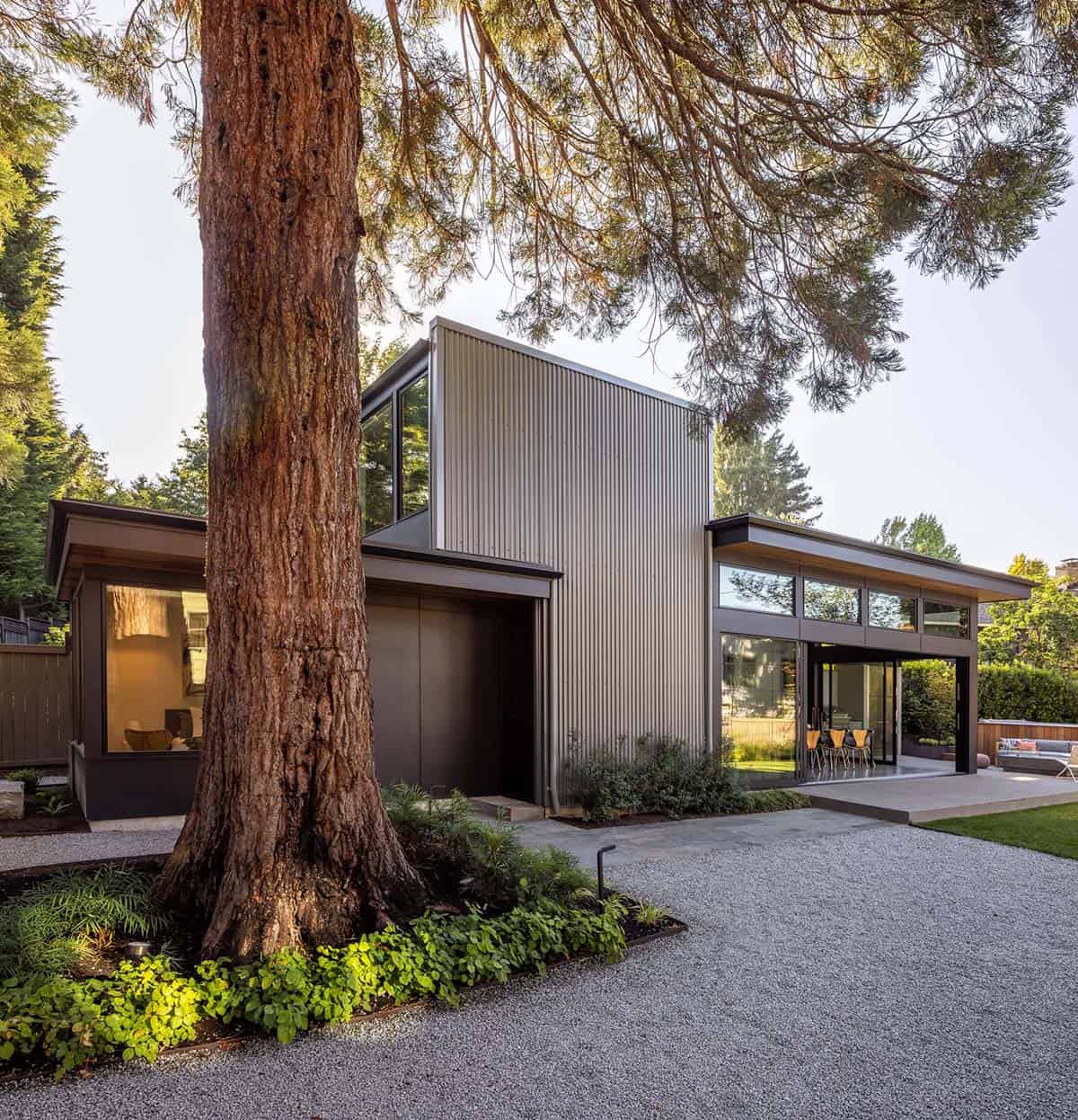 Quincho structure under a mature sequoia, metal and wood volumes with glass doors open to a stone patio