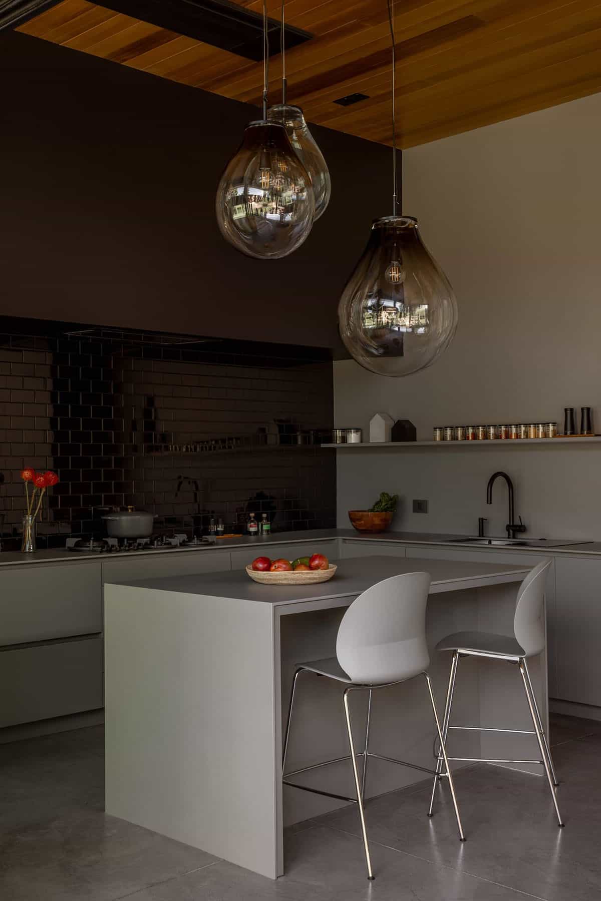 Moody kitchen with black subway tile and two amber glass pendant lights over the island