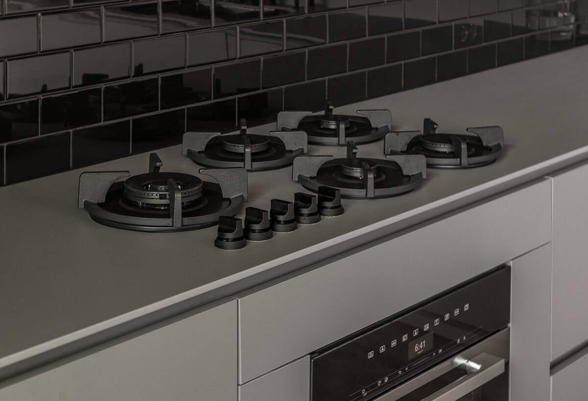 Close-up of a five-burner black gas cooktop in a gray stone countertop