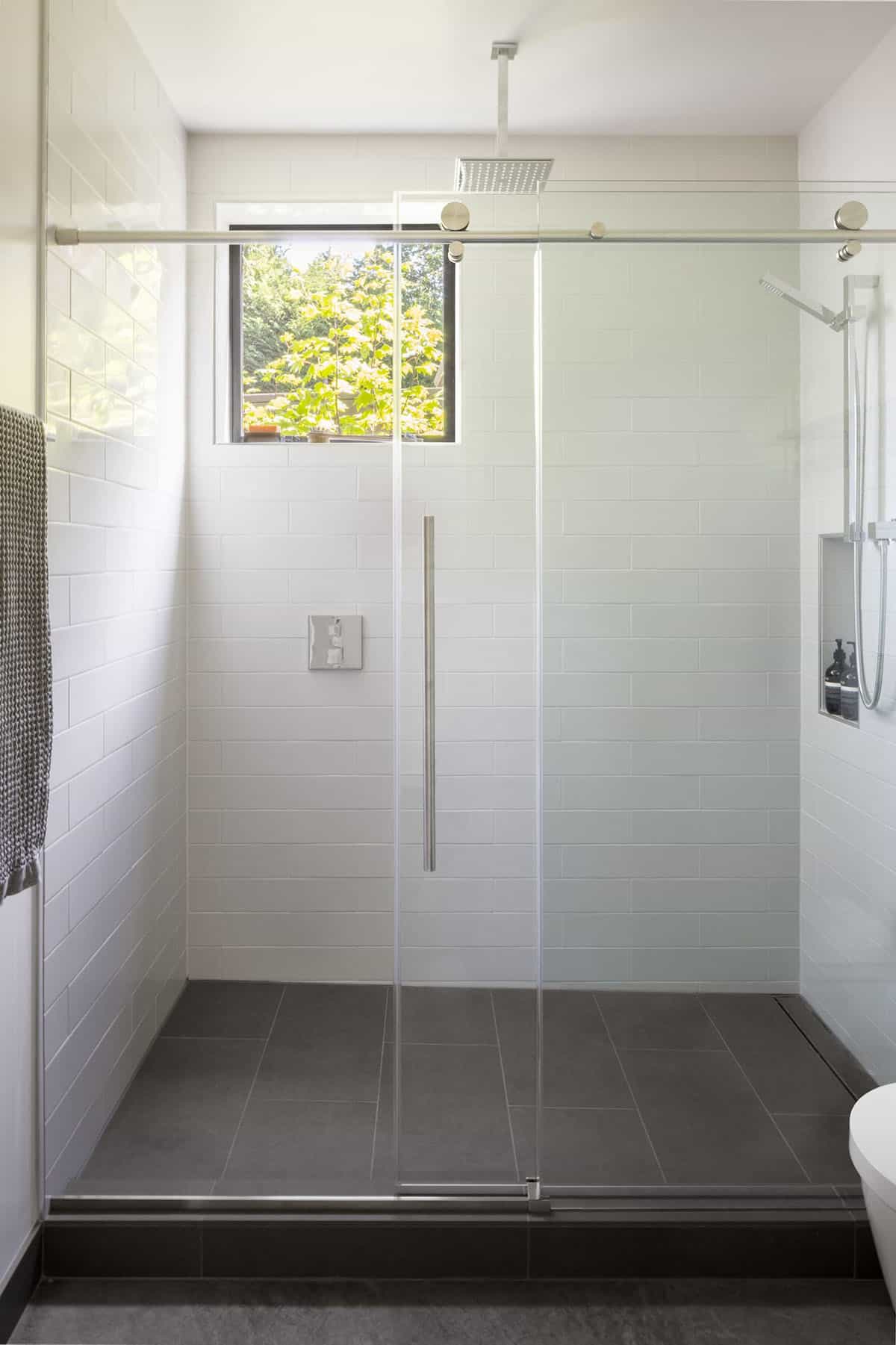 Glass-enclosed shower with white subway tile, dark floor tile, and a rainfall head