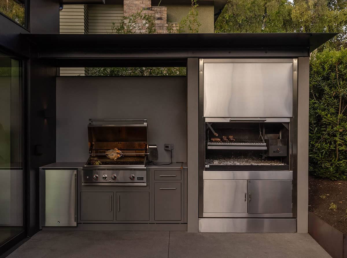Outdoor kitchen with a built-in gas grill roasting a chicken and a wood-fired grill beside it