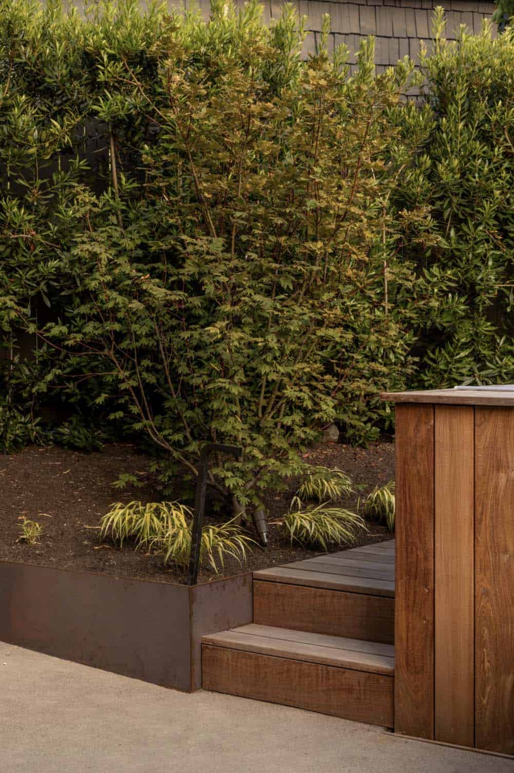 Corten steel garden edge and wood deck steps leading to the hot tub, framed by a hedge