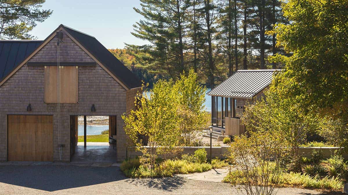 Exterior of a shingled barn-style structure with wood doors, overlooking a lake through the trees